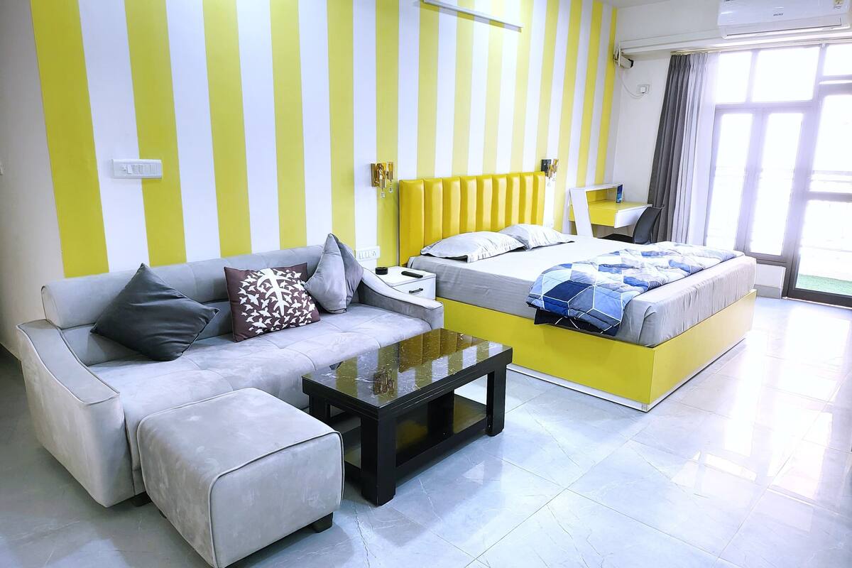 Una habitación de hotel moderna con sofá, cama, una mesita y ventana con cortinas.