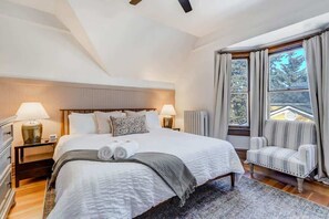 Un dormitorio espacioso con una cama grande, dos mesitas de noche con lámparas, una ventana con cortinas y vistas al exterior.