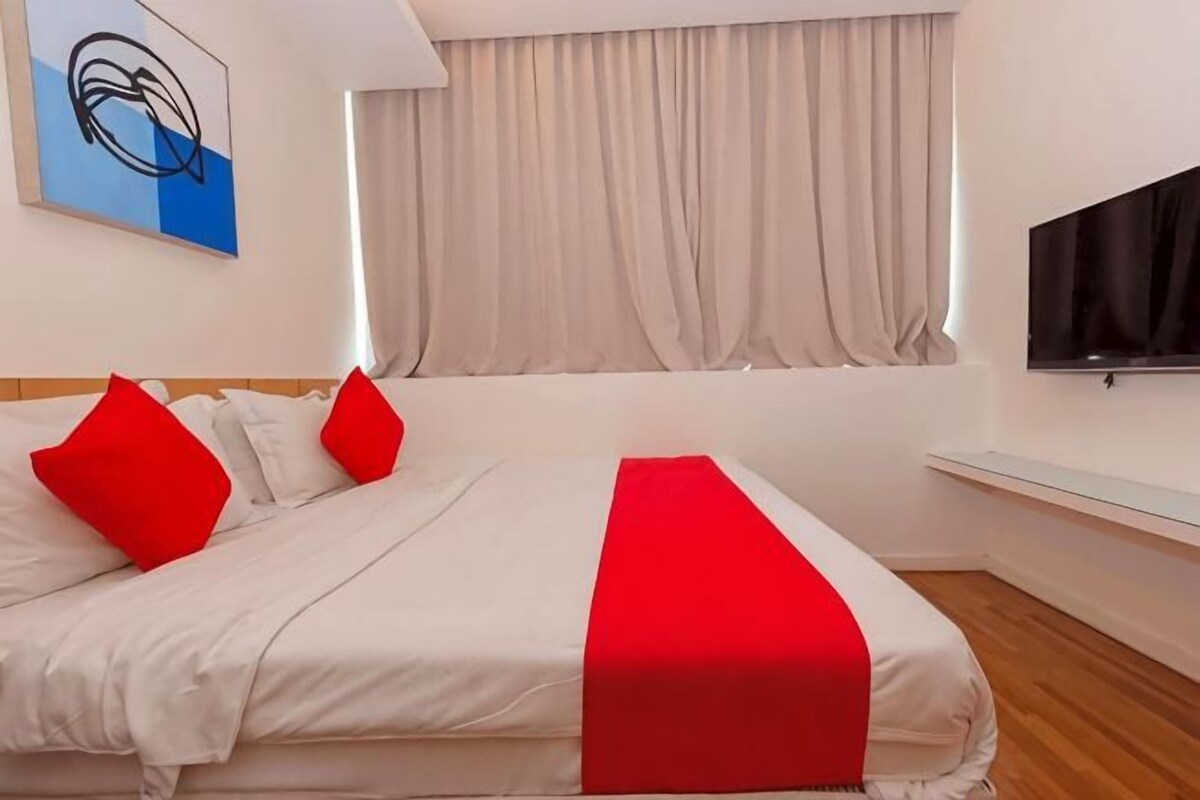 A hotel room with a large bed, a TV mounted on the wall, and a window with curtains.