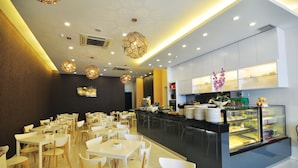 A modern restaurant with white tables and chairs, a central counter with a display case, and decorative hanging lights. - Mio Boutique Hotel Melaka (Malacca City)