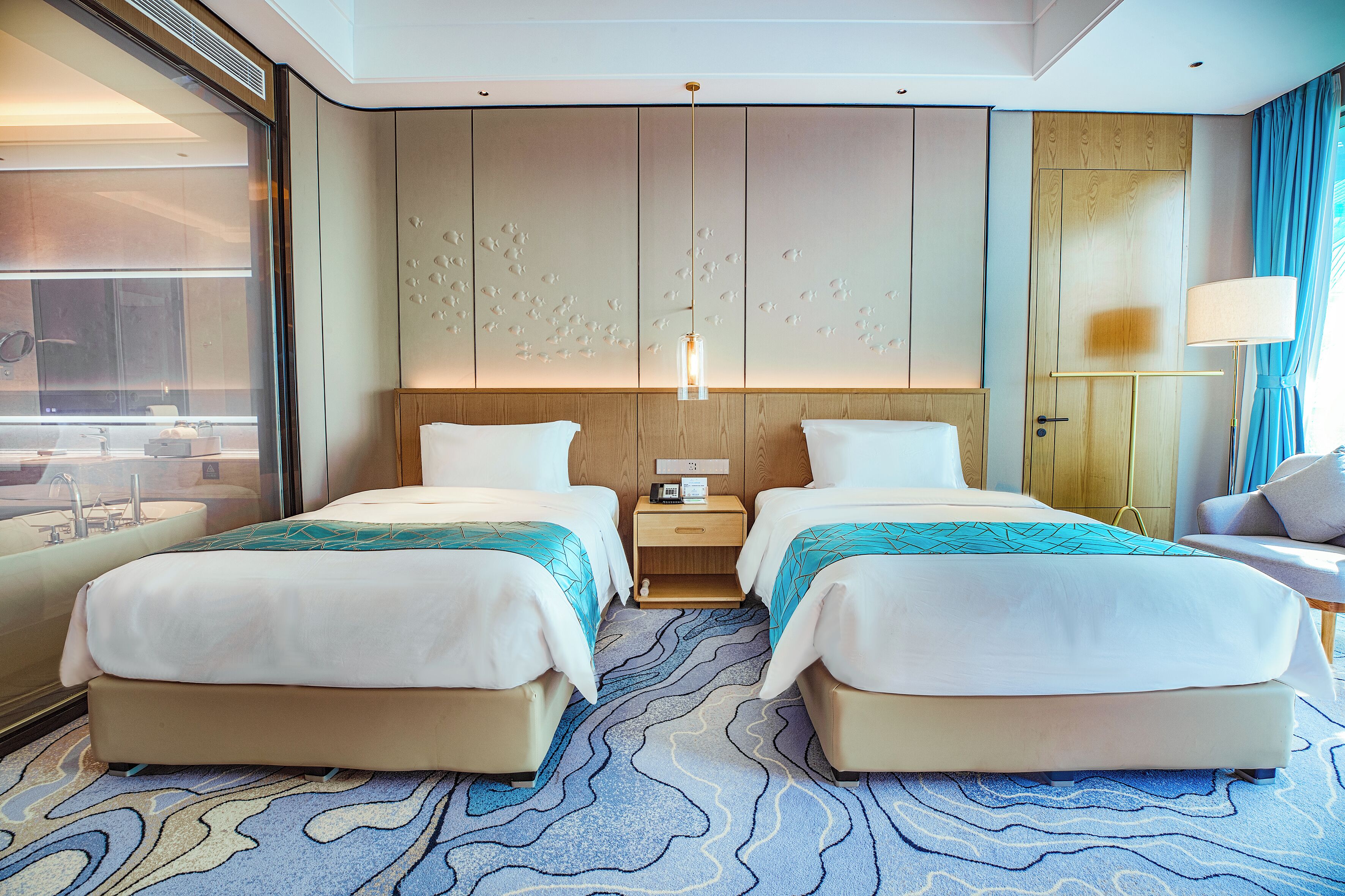 Een hotelkamer met twee bedden, een nachtkastje, een lamp en uitzicht op de stad.