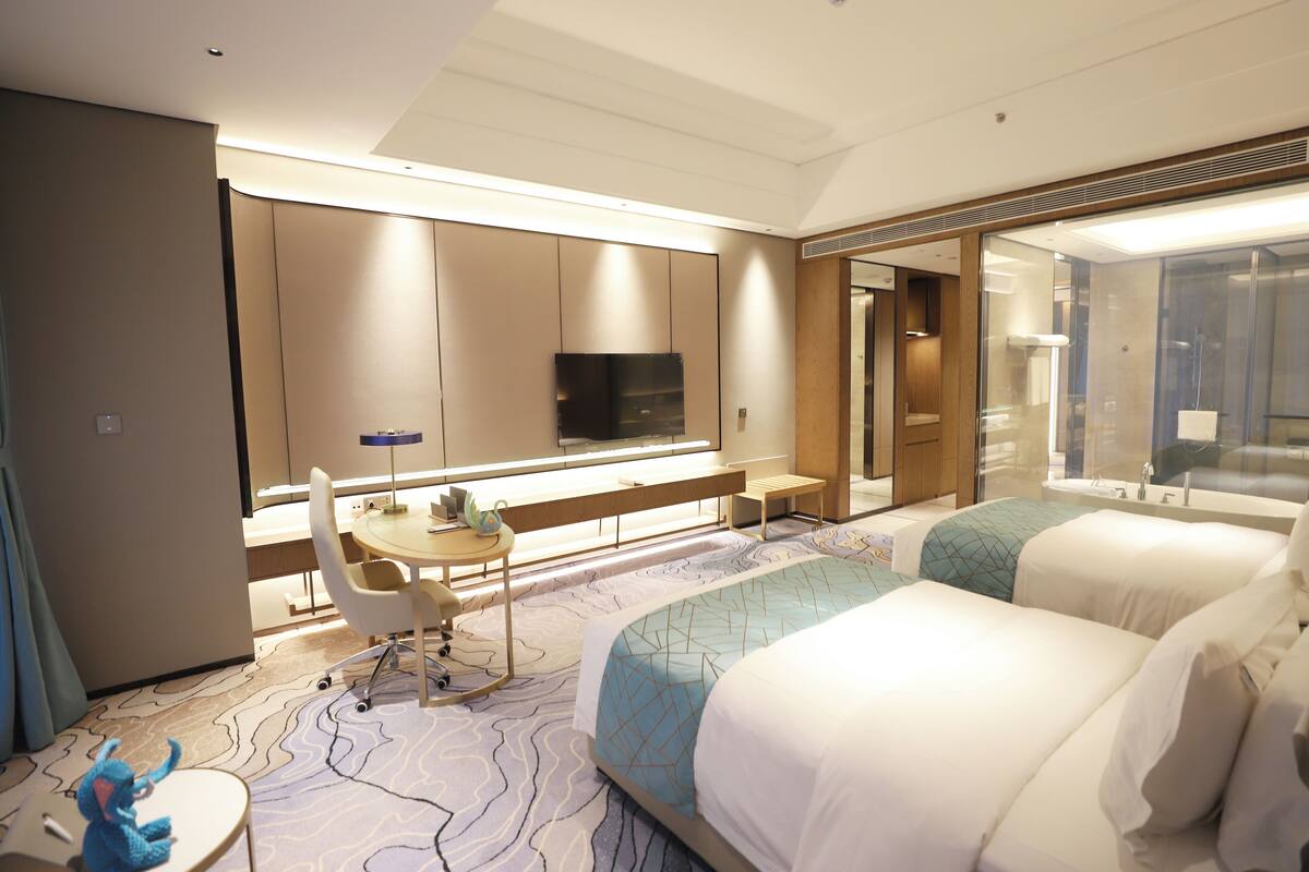 Ein Hotelzimmer mit Bett, Schreibtisch mit Stuhl, Fernseher und Badezimmer mit Spiegel.