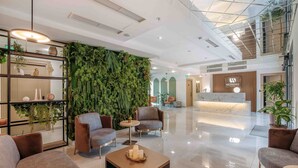 Un hall d’hôtel moderne comprenant un comptoir d’accueil, un espace salon et un mur végétal.