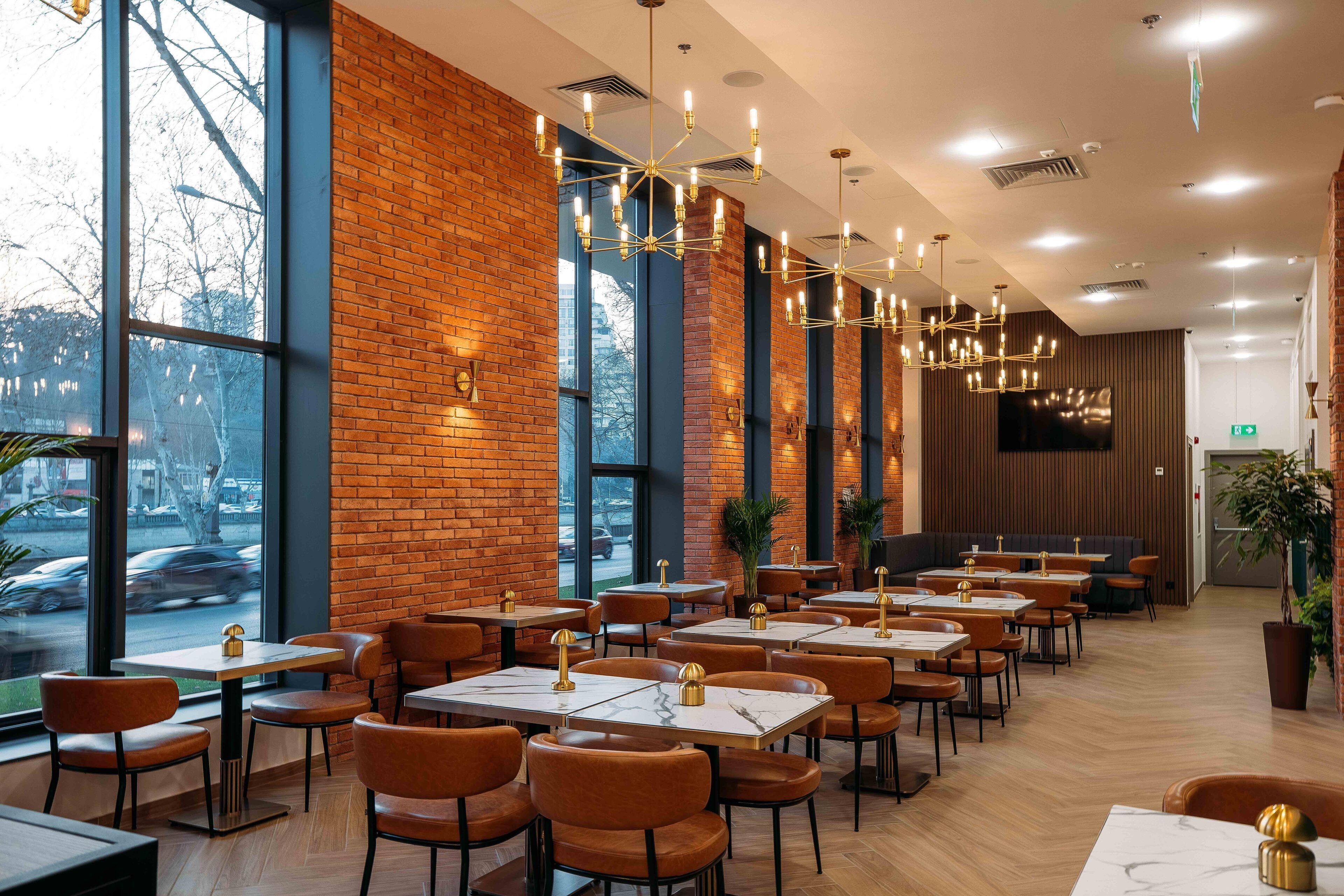 Un restaurant moderne avec des murs en briques, de grandes fenêtres et différents types de mobilier pour créer des espaces de détente variés.