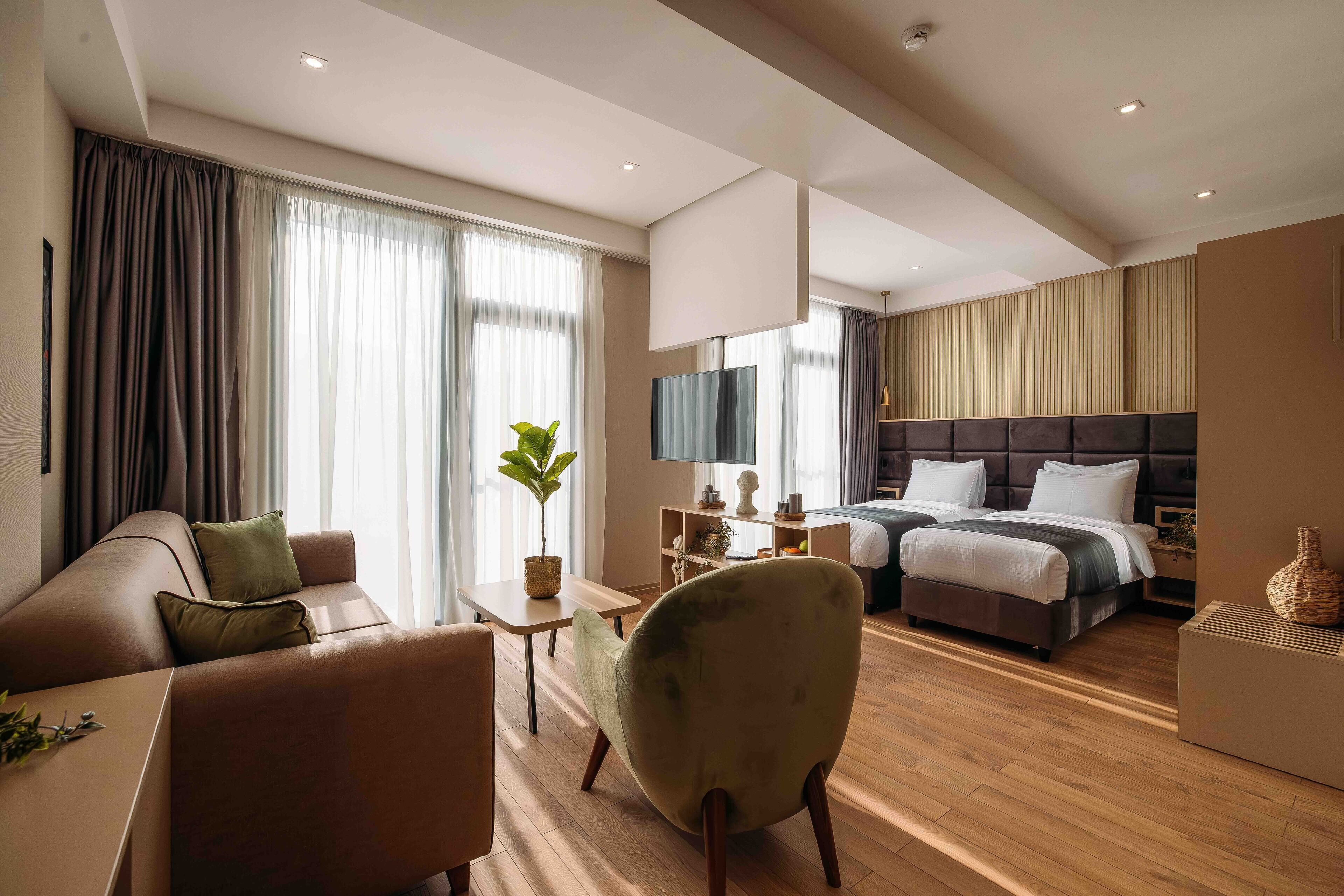 Quarto de hotel moderno com sofá, poltrona, mesa de jantar e cama com cabeceira.