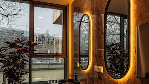 Une salle de bain moderne avec une grande fenêtre, une plante en pot et un meuble-lavabo doté de deux miroirs et d’un évier.