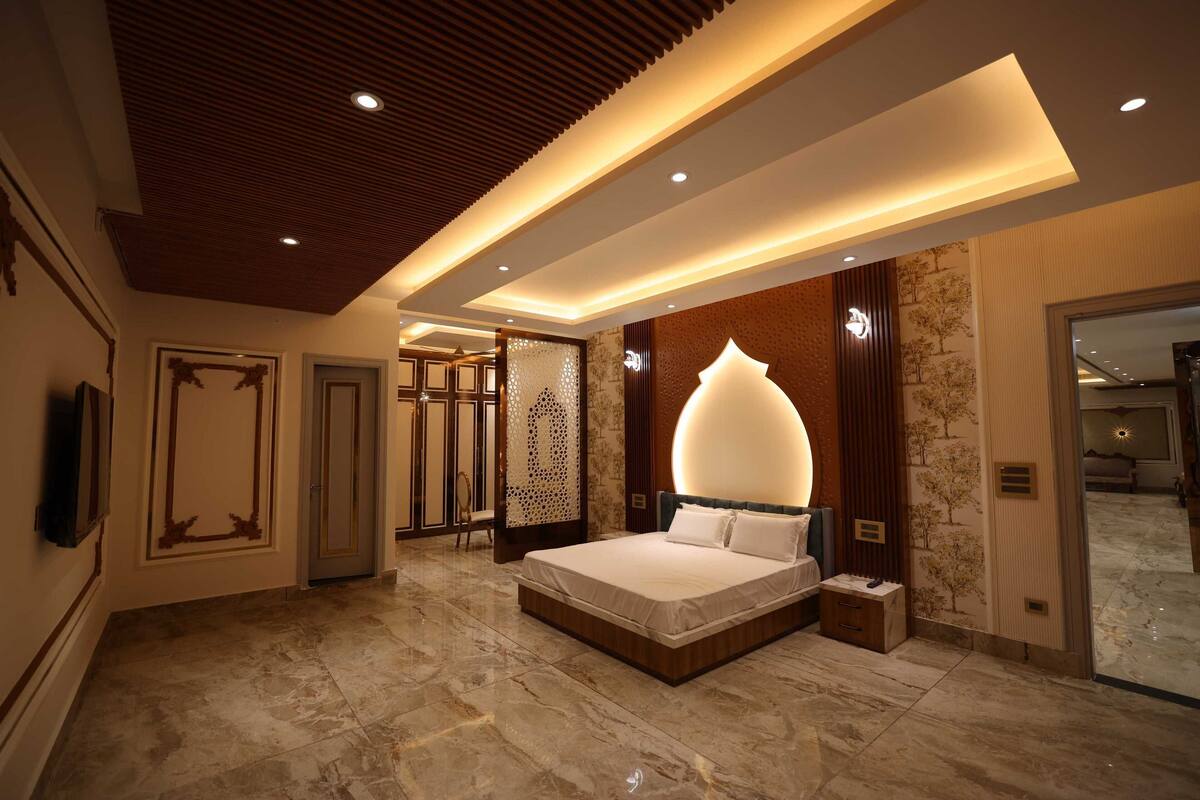 A modern bedroom with a large bed, recessed lighting, and a decorative wall panel.