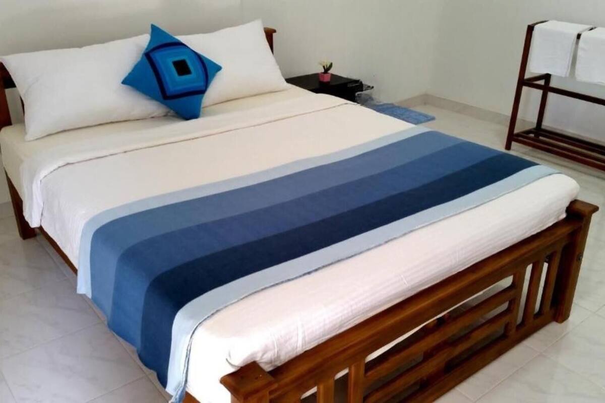 Una cama con colcha a rayas, cabecera de madera y mesita de noche con lámpara.