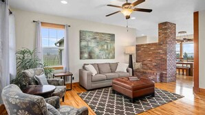 A spacious living room with a grey sofa, patterned armchairs, a brown ottoman, a large abstract painting, and a ceiling fan. - Picturesque Vineyard and Valley Views, Quiet and Private Setting, Huge Deck, *Complimentary Wine* (Newberg)