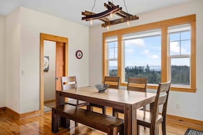 A dining area with a wooden table and benches, large windows with a view of a forest, and a modern pendant light.