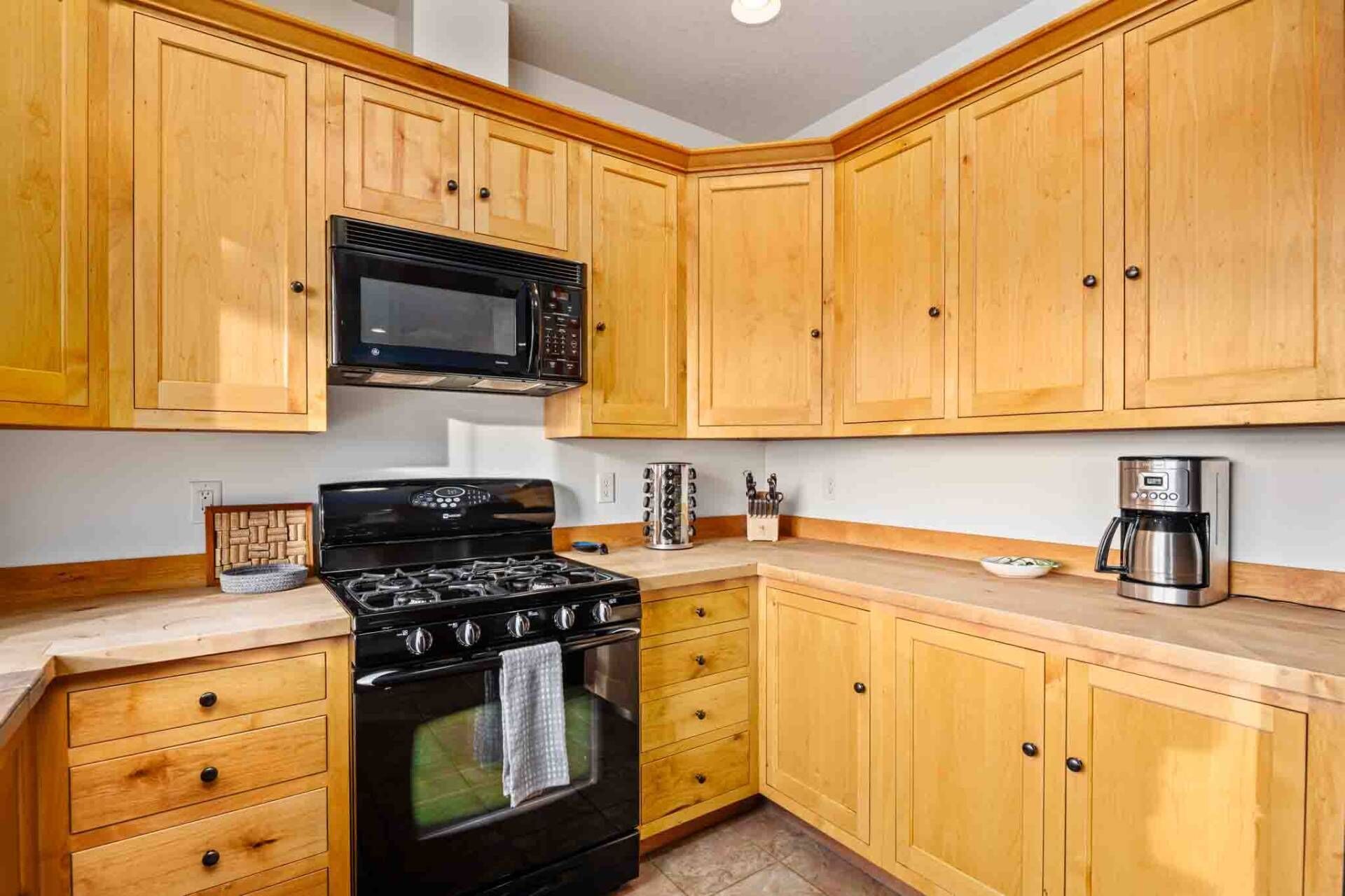 A kitchen with wooden cabinets, a black stove, a microwave, and a coffee maker.