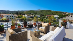 Una terraza en la azotea con mobiliario de mimbre, plantas en macetas y vistas a un pueblo y colinas.
