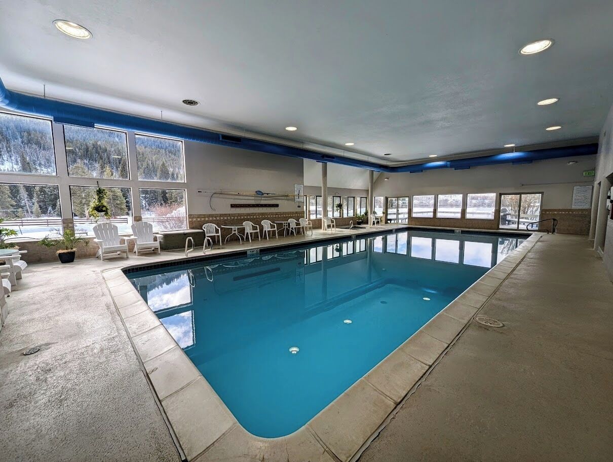 An indoor swimming pool with clear blue water, surrounded by white chairs and potted plants.