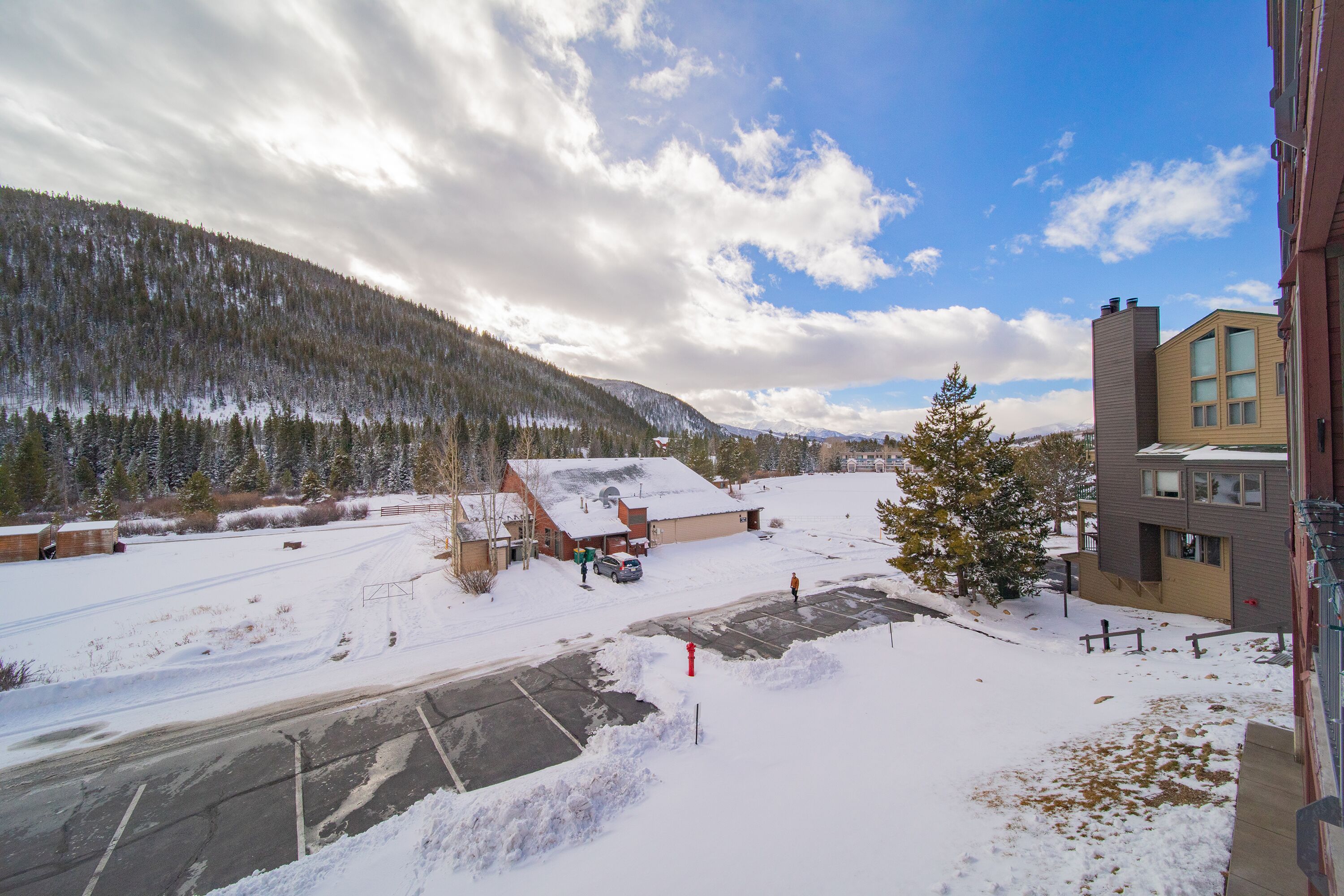 A snow-covered parking lot with buildings and a forested mountain in the background.