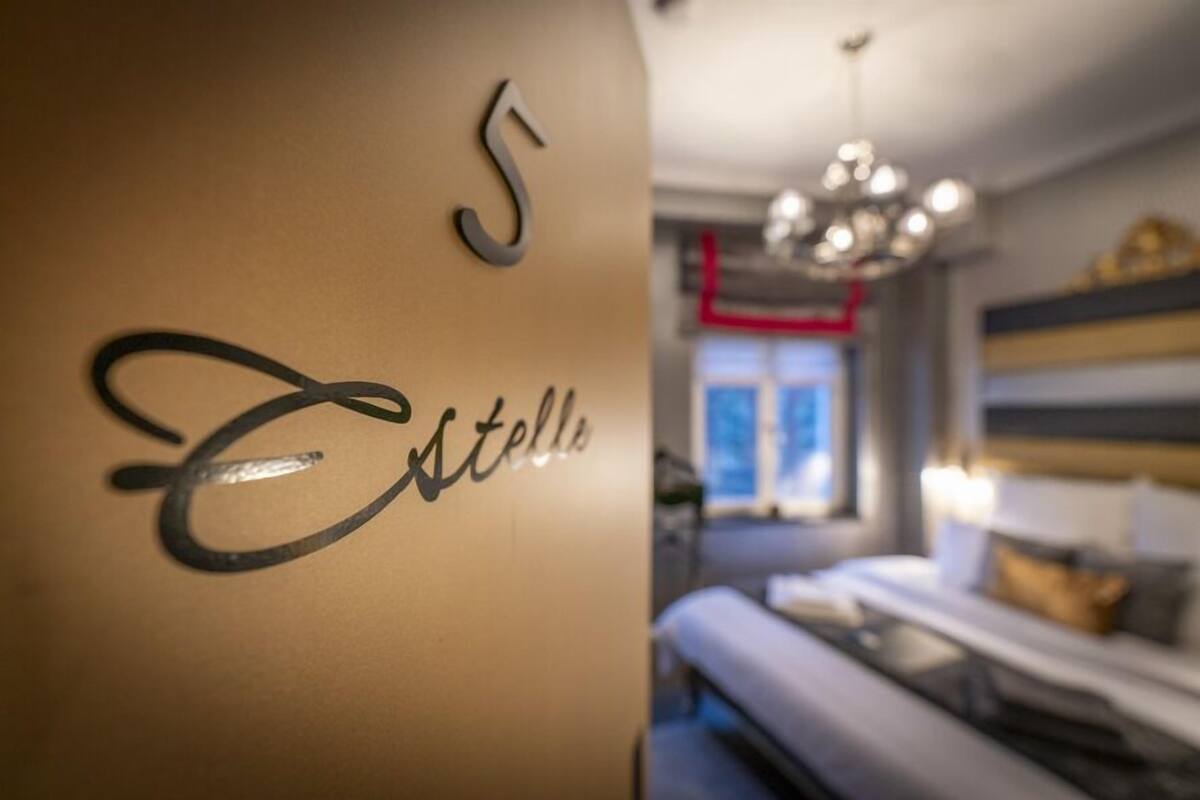 Habitación de hotel con cama, candelabro y pared con el número '5' y la palabra 'Estelle'.