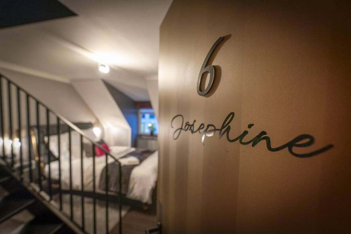 Habitación de hotel con una escalera, una cama y una pared con el número 6 y el nombre 'Josephine' escrito.