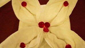 Almohada blanca con pétalos de rosa roja dispuestos en forma de flor.
