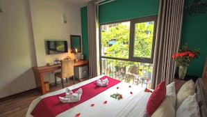 Habitación de hotel con cama, escritorio, silla, televisión y balcón con vistas a zonas verdes.