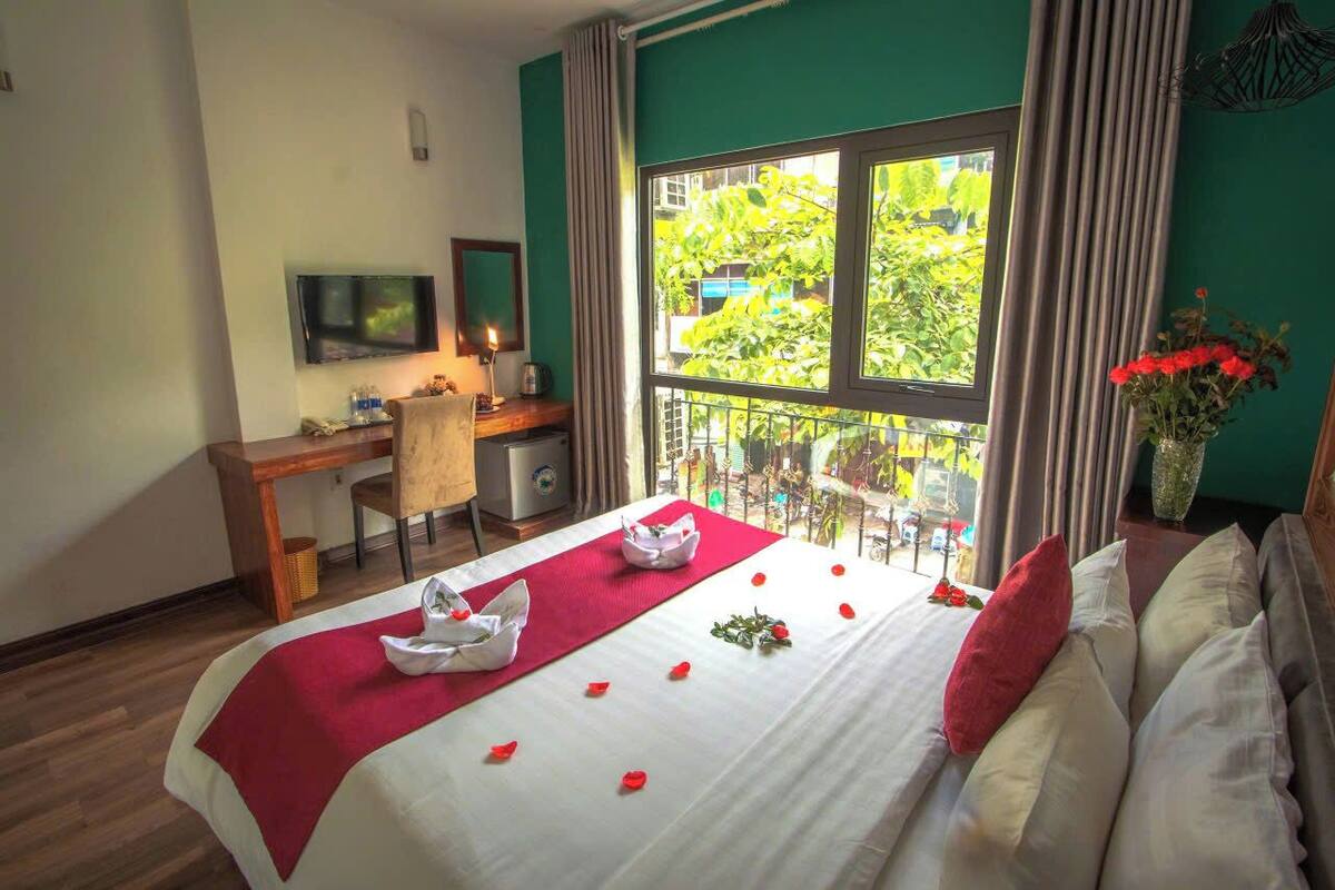 Habitación de hotel con cama, escritorio, silla, televisión y balcón con vistas a zonas verdes.