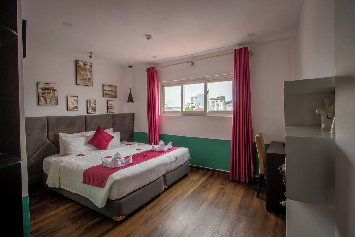 Un dormitorio con cama, escritorio, silla y ventana con cortinas.