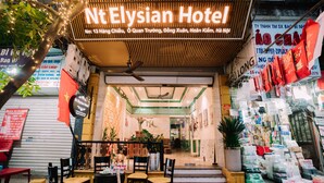 Exterior del hotel Nt Elysian, con un cartel, área de estar al aire libre y diversas tiendas.