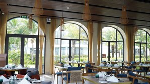 Un restaurante con mesas y sillas, ventanas amplias y vistas a zonas verdes.