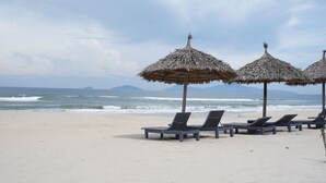 Una playa con sombrillas de paja y sillones reclinables.