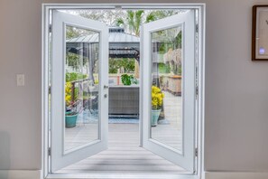A glass door leading to an outdoor patio with potted plants and a pergola. - Arpieka Garden (St. Augustine)