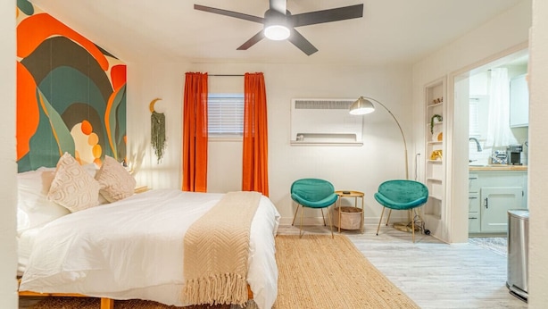 A bedroom with a bed, a ceiling fan, a window with curtains, a bedside table, and a chair. - Riverside Luxe: Stylish Designer Retreat (Reno)