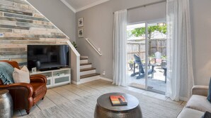 Una sala de estar con televisor, sofá de cuero y una escalera que lleva a un balcón con mobiliario exterior.