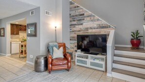 Una sala de estar con chimenea, un sillón de cuero, un televisor y una escalera.