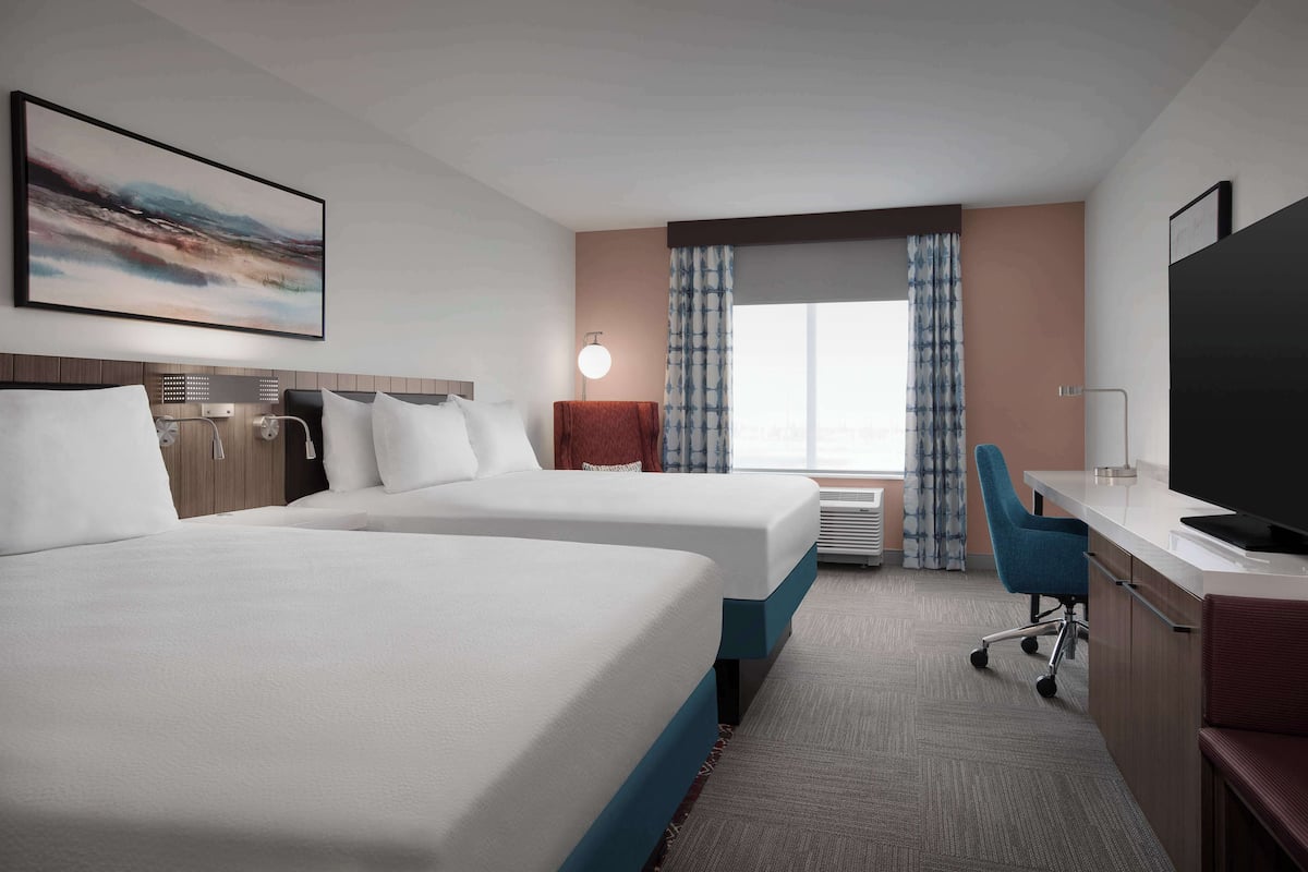 A hotel room with two beds, a desk, a TV, and a window with curtains.