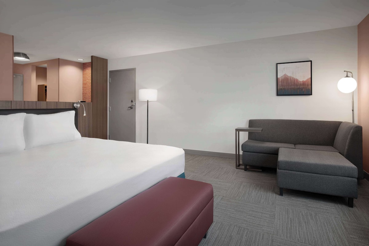 A hotel room with a bed, a sofa, a small table, a lamp, and a door.