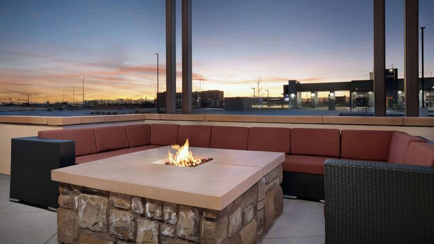An outdoor seating area with a stone fire table and cushioned benches, overlooking a cityscape at dusk.