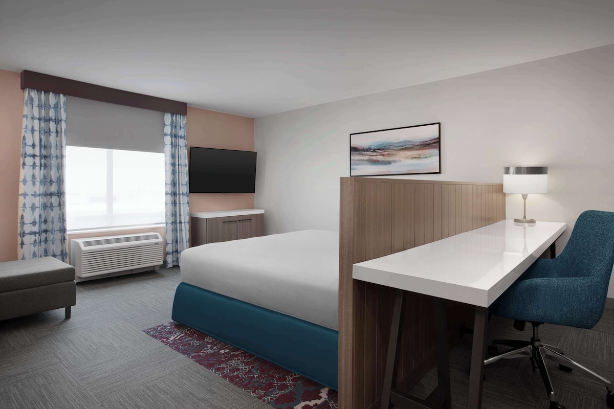 A hotel room with a bed, a desk, a chair, a TV, and a window with curtains.