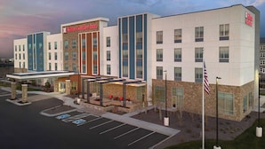 A modern hotel with a prominent Hilton Garden Inn sign, a covered outdoor seating area, and a flagpole with an American flag.