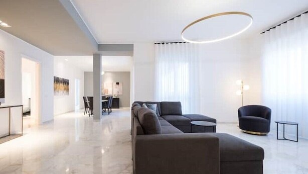 A modern living room with a sectional sofa, a round coffee table, and a black armchair. - Spacious penthouse with gym in historic building, near the Colosseum (Roma)