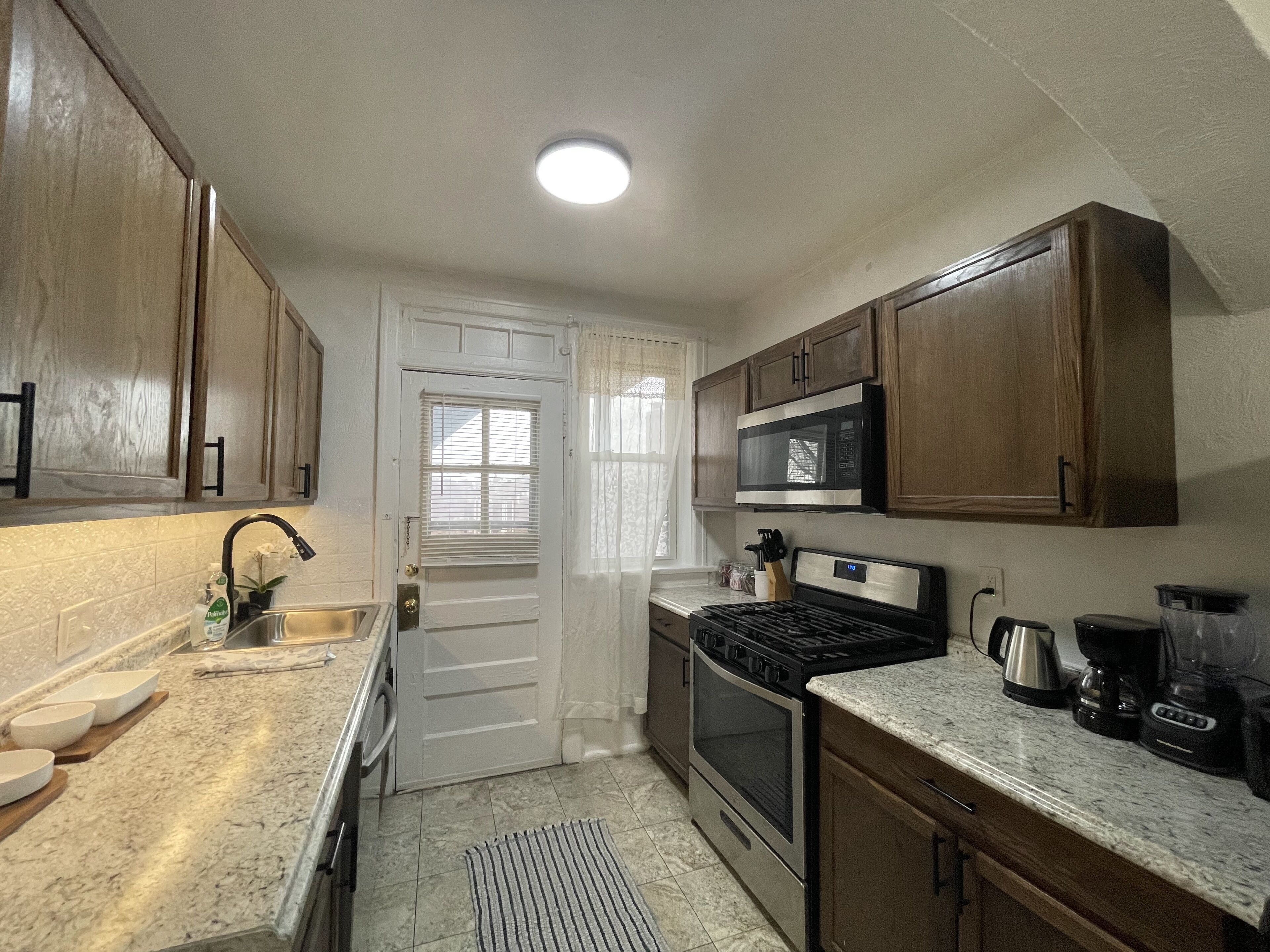 A kitchen with wooden cabinets, a stainless steel sink, a microwave, a stove, and a coffee maker.