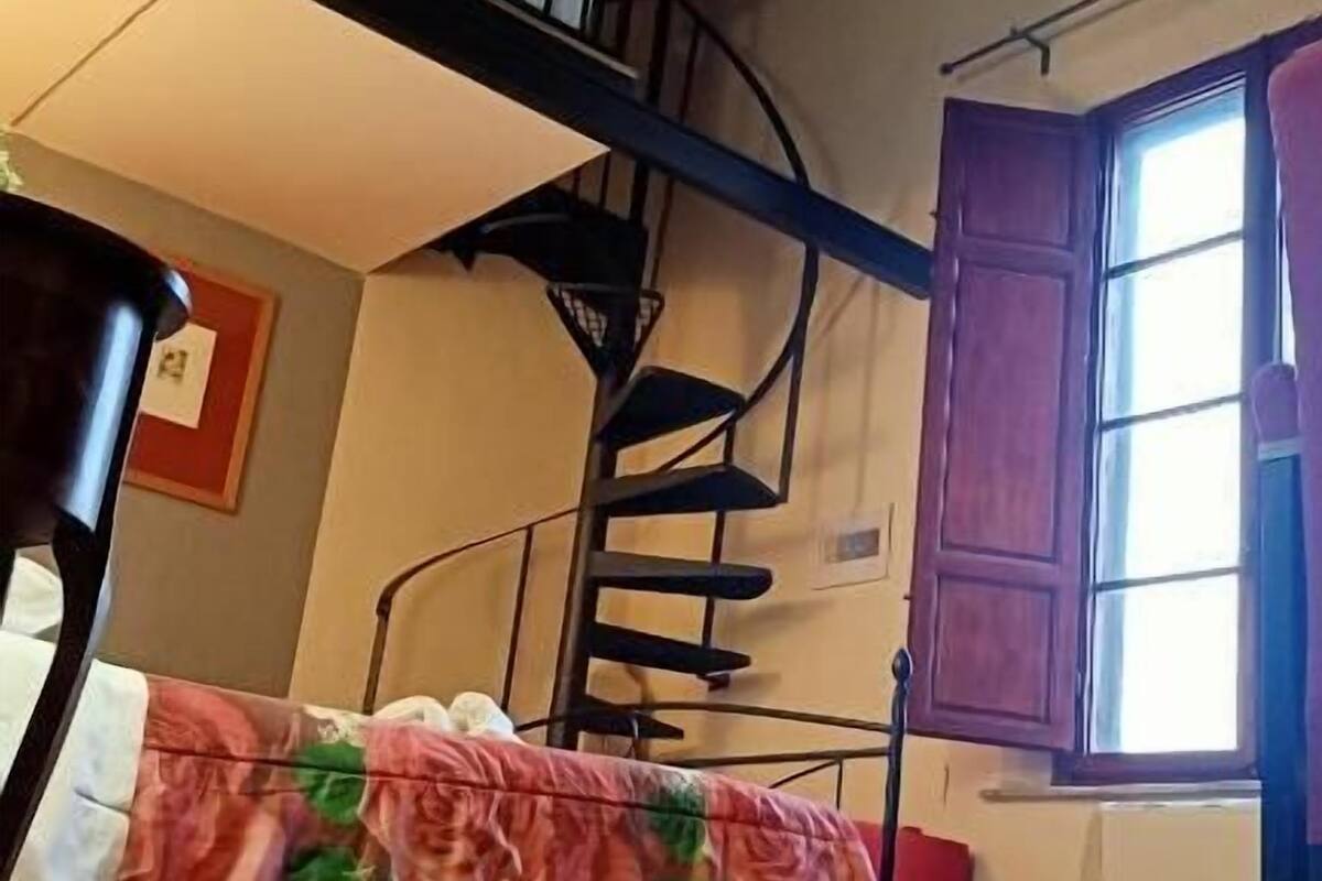 A room with a spiral staircase, a bed with a floral bedspread, a window with a view, and a radiator.