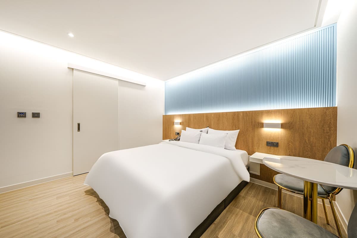 Una habitación de hotel moderna con una cama grande, mesitas de noche, una pequeña mesa redonda y una silla.