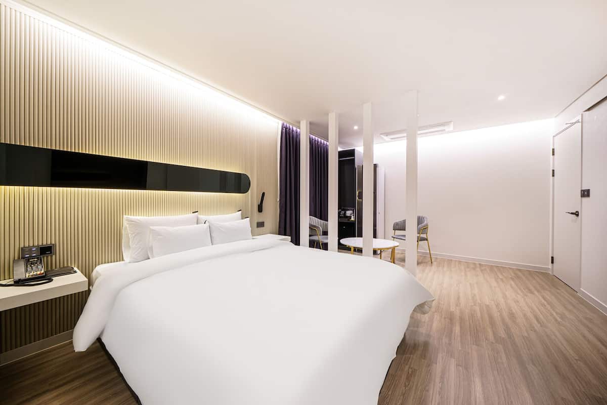 Una habitación de hotel moderna con una cama grande, una mesita de noche con cafetera, un escritorio y una silla.