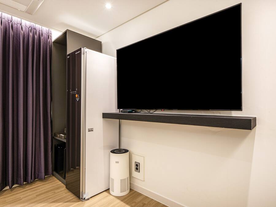 A modern room with a flat-screen TV mounted on a wall, a built-in air conditioning unit, and a sliding door.