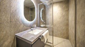 A modern bathroom with a granite countertop sink, a large mirror, and a glass shower enclosure.