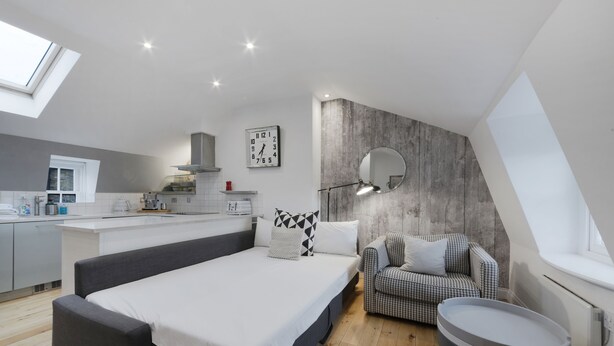 Une chambre de style loft moderne, dotée d’un grand lit, d’un coin salon, d’une cuisine à l’arrière-plan et d’une fenêtre de toit.