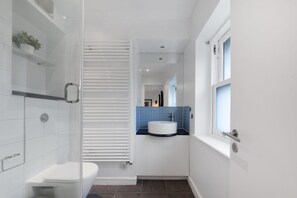 Ein modernes Badezimmer mit Duschkabine aus Glas, einer weißen Toilette und einem Waschbecken mit blauer Ablagefläche.