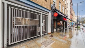 Un commerce fermé, avec une grille métallique, un bâtiment en briques et un trottoir mouillé.