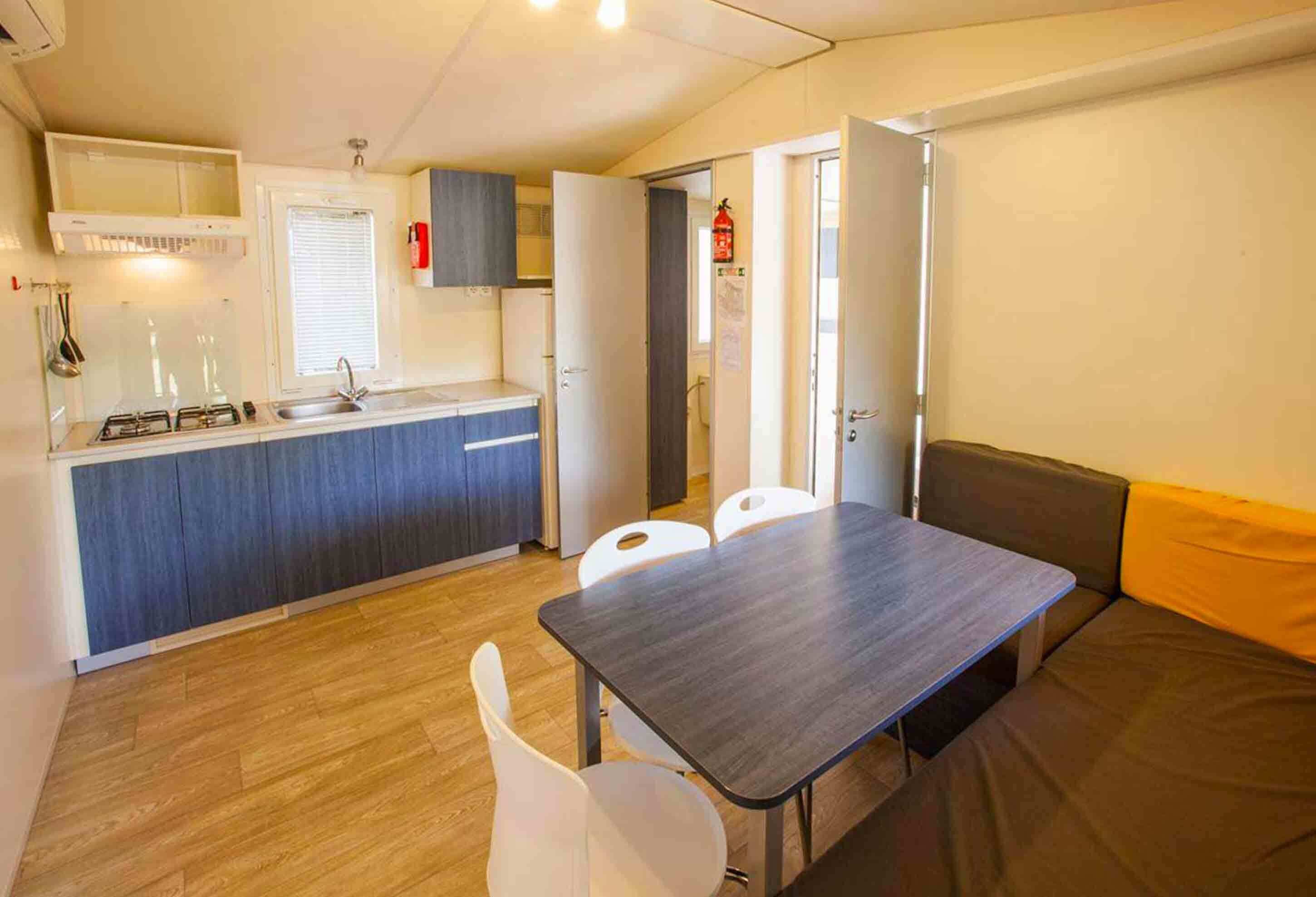 A compact kitchen with a sink, stove, and cabinets, a dining table with chairs, and a sofa.