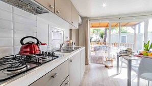 A modern kitchen with a gas stove, a kettle, and a sink. There is a dining area with a table and chairs, and a view of a deck and outdoor furniture. - Baia Holiday Gasparina (Castelnuovo del Garda)