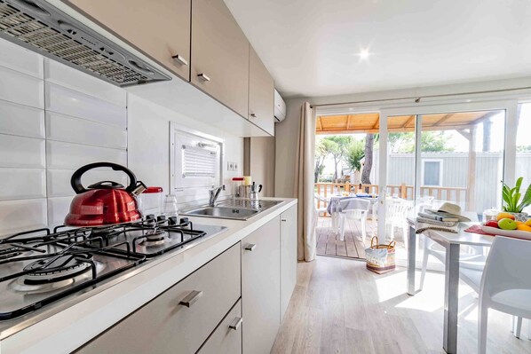 A modern kitchen with a gas stove, a kettle, and a sink. There is a dining area with a table and chairs, and a view of a deck and outdoor furniture.
