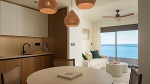 A modern kitchen with pendant lights, a dining area with a round table, and a view of the sea through large windows.